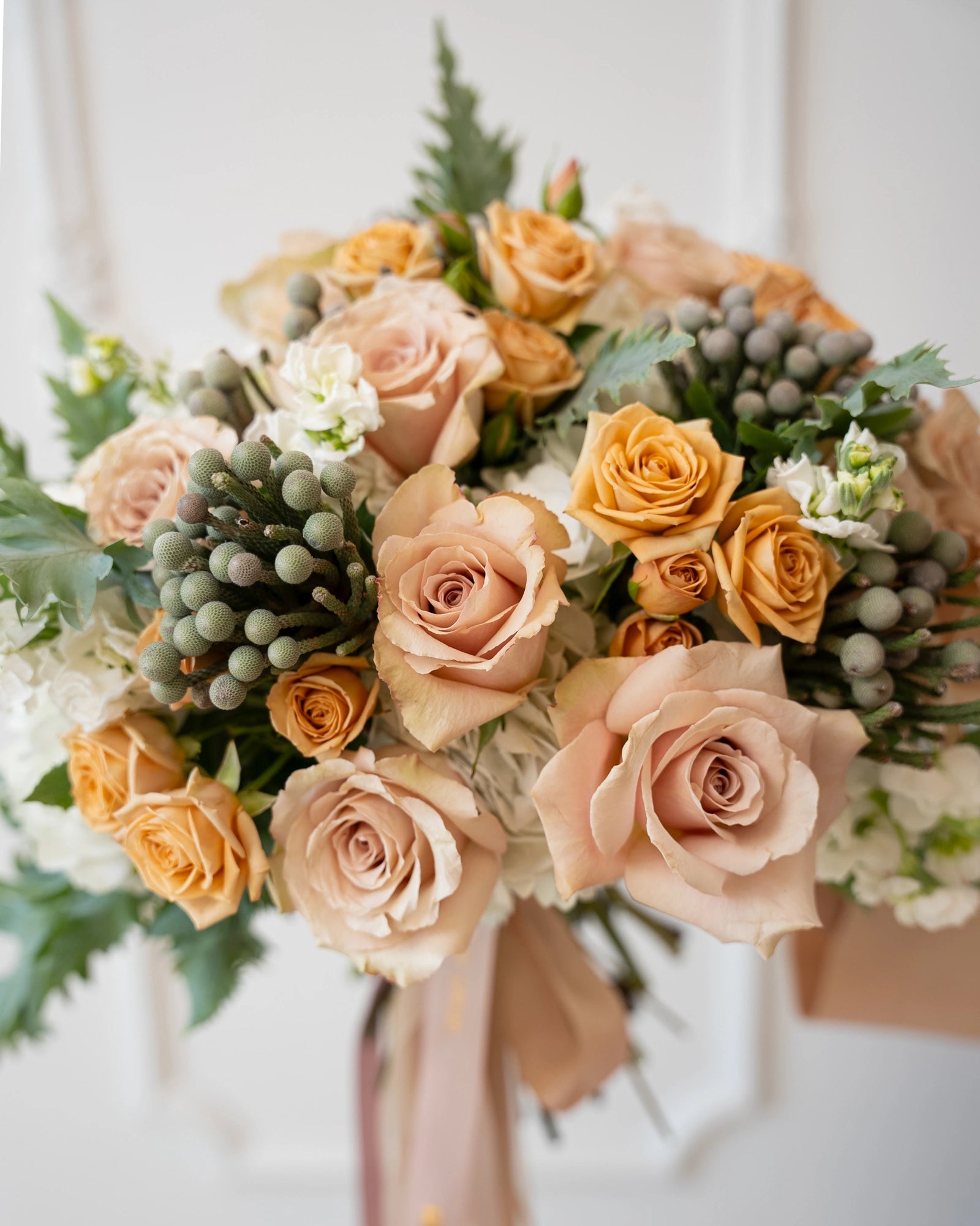 Closeup of peach and blush roses clustered with hydrangea and brunia accents