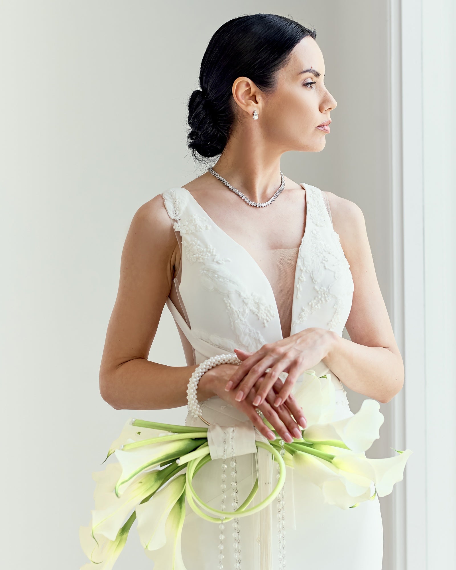 Modern bridal bouquet designed as a sculptural purse with white calla lilies, pearl handle, and crystal tassel chains, held by a bride in an elegant gown.