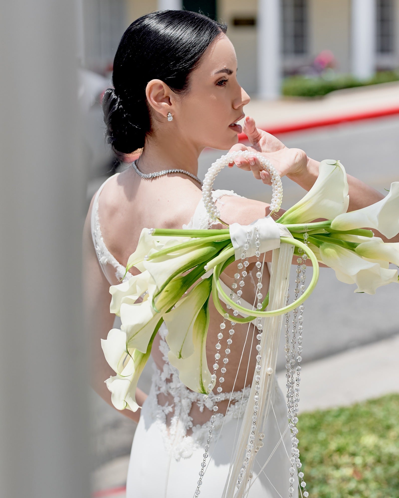 Modern bridal bouquet designed as a sculptural purse with white calla lilies, pearl handle, and crystal tassel chains, held by a bride in an elegant gown.