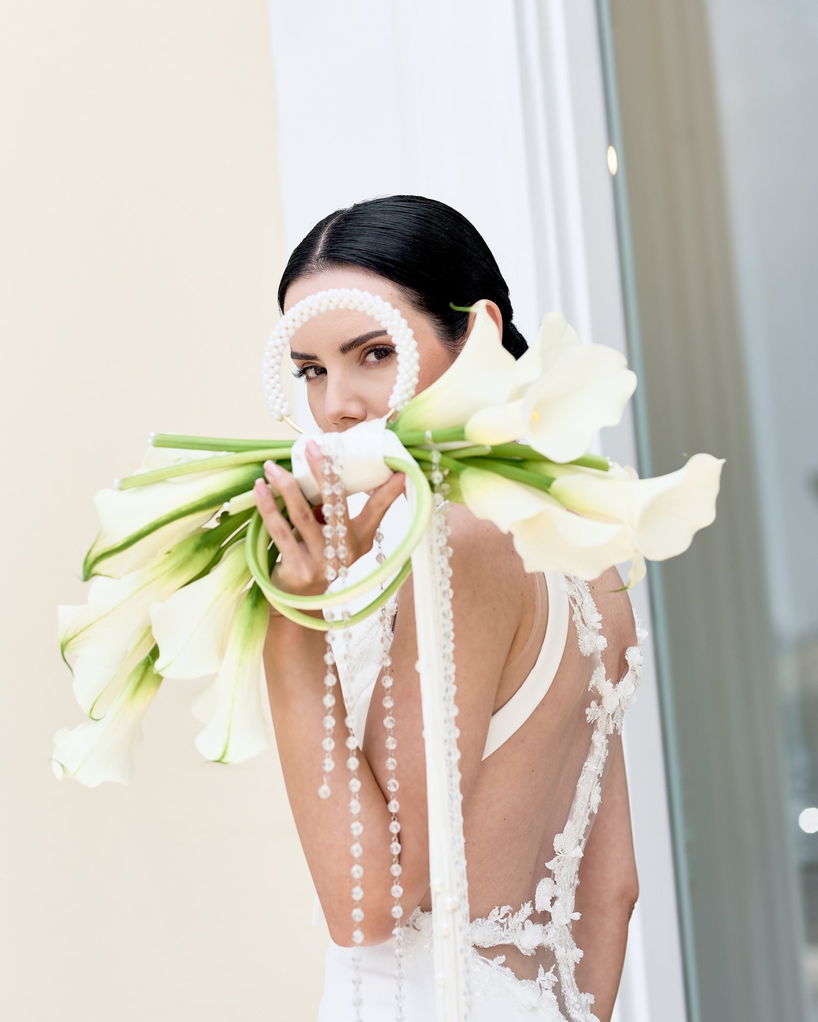 Modern bridal bouquet designed as a sculptural purse with white calla lilies, pearl handle, and crystal tassel chains, held by a bride in an elegant gown.