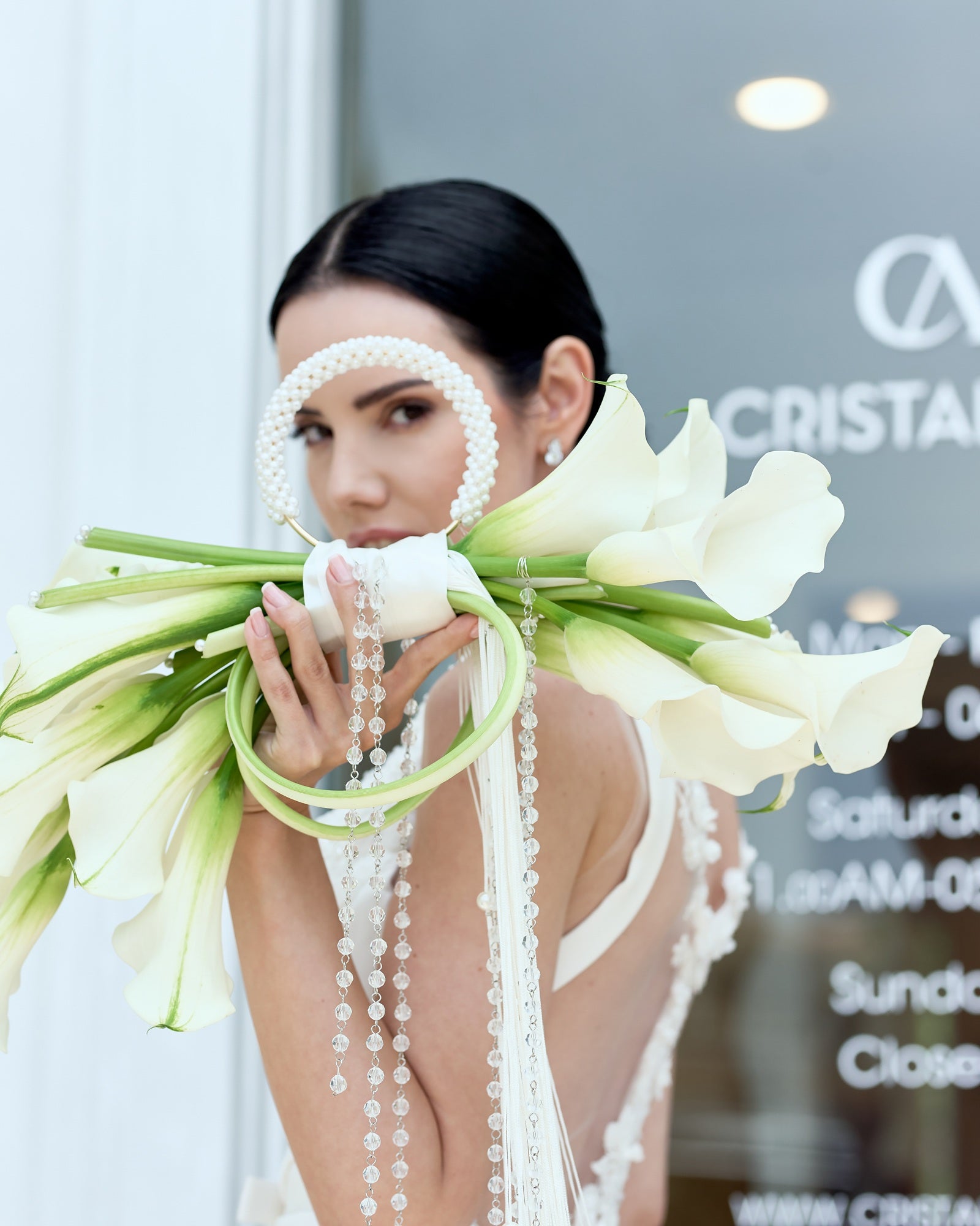 Modern bridal bouquet designed as a sculptural purse with white calla lilies, pearl handle, and crystal tassel chains, held by a bride in an elegant gown.
