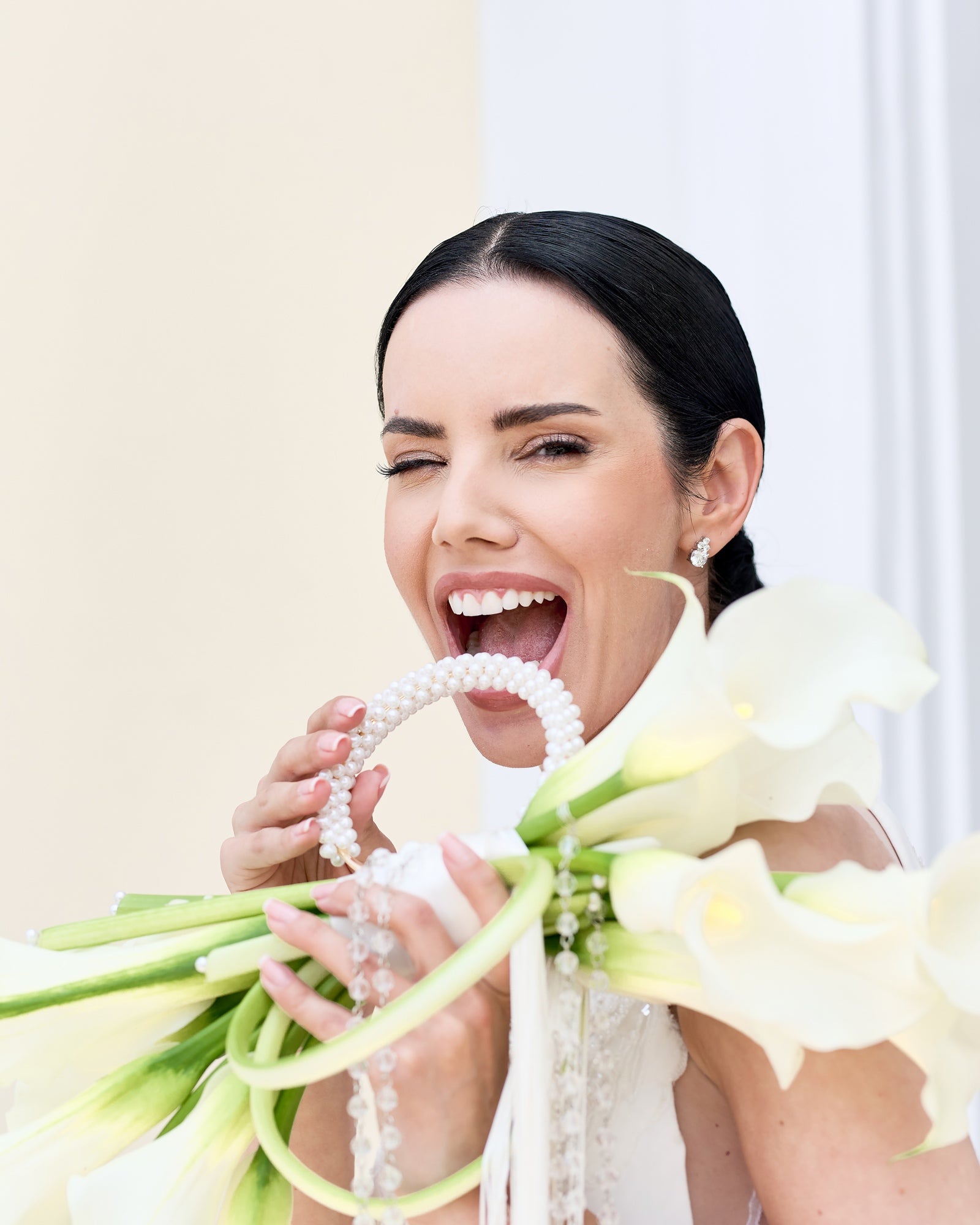 Modern bridal bouquet designed as a sculptural purse with white calla lilies, pearl handle, and crystal tassel chains, held by a bride in an elegant gown.
