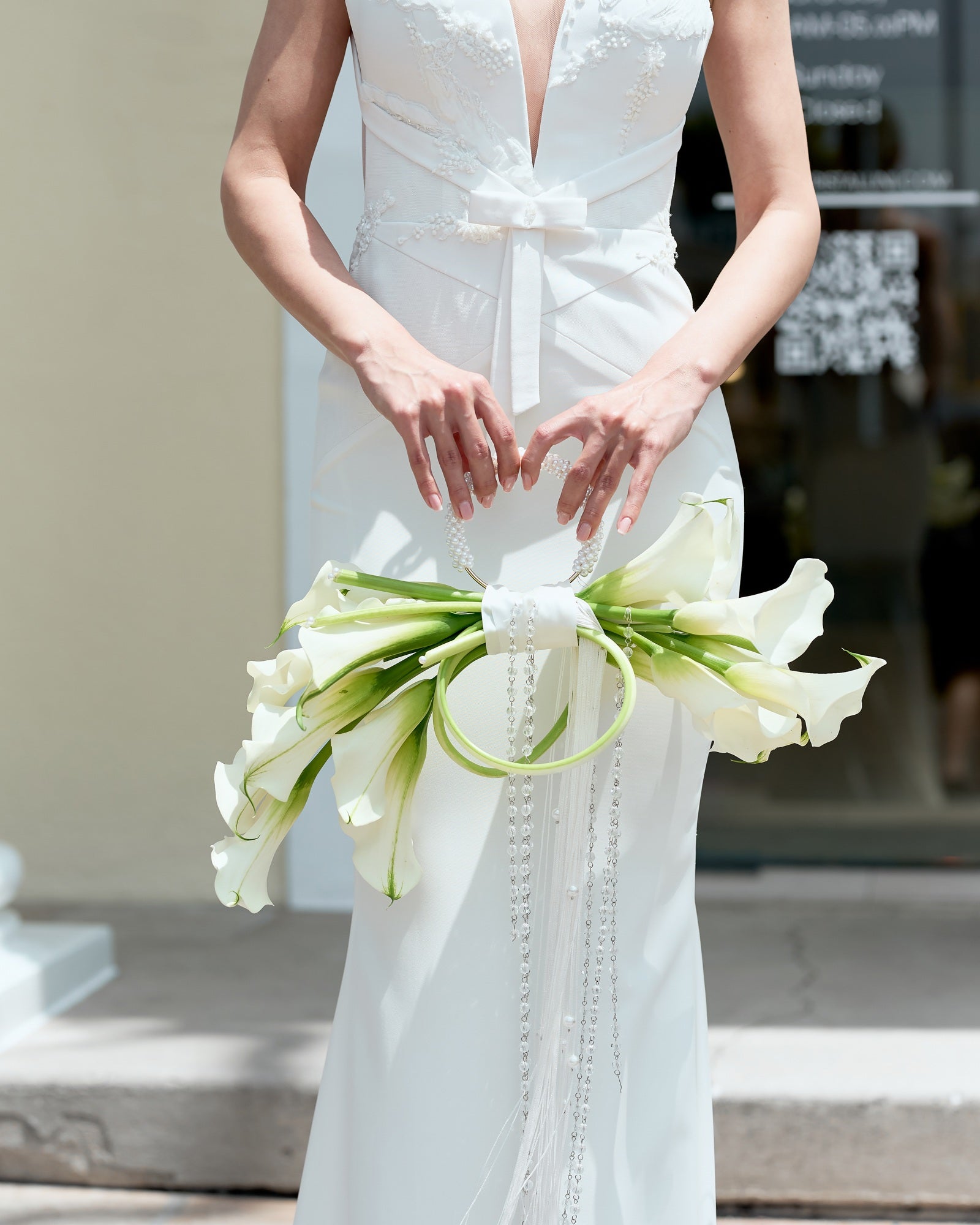Modern bridal bouquet designed as a sculptural purse with white calla lilies, pearl handle, and crystal tassel chains, held by a bride in an elegant gown.