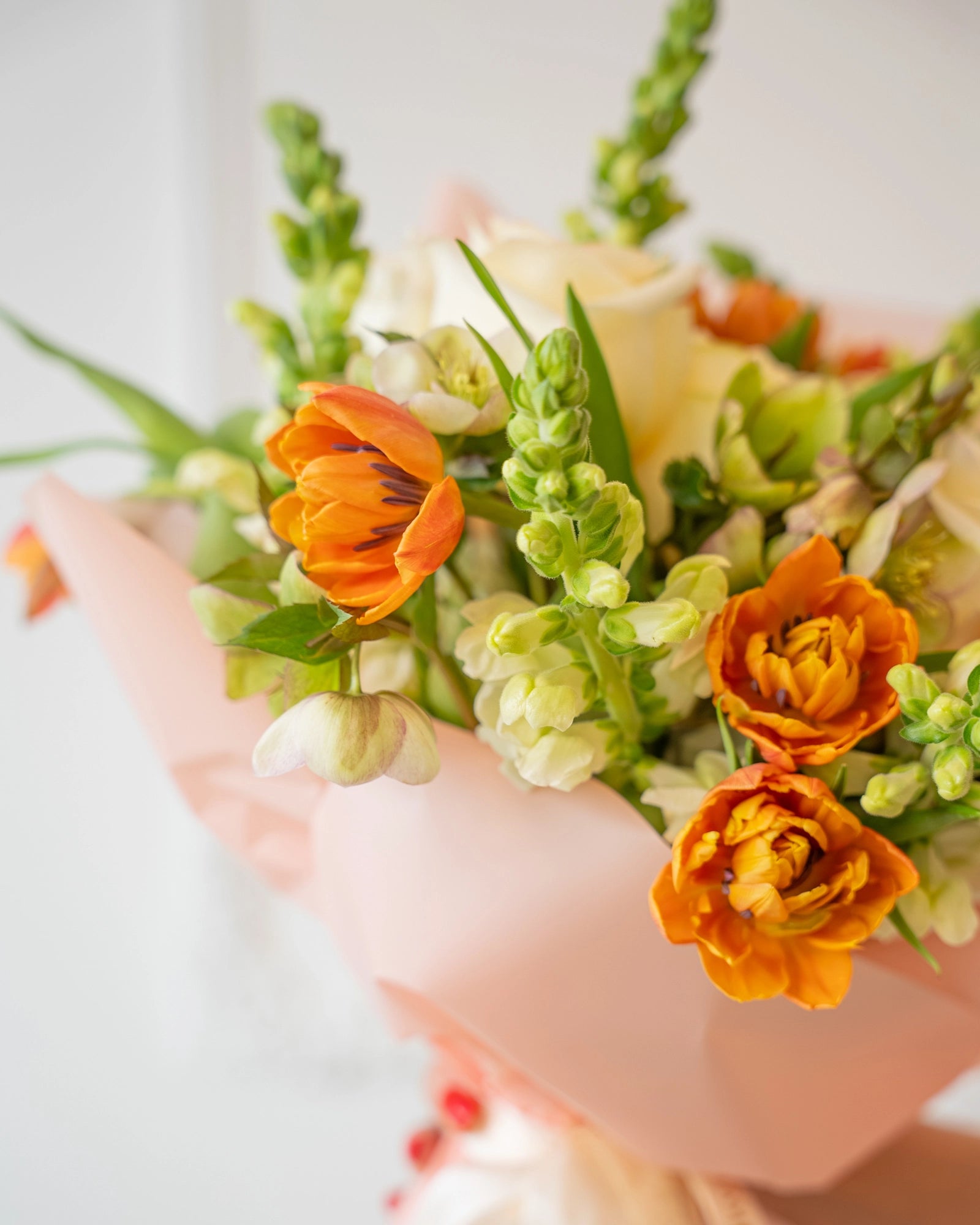 Closeup of orange tulips, cream roses and snapdragons arranged in soft blush paper.