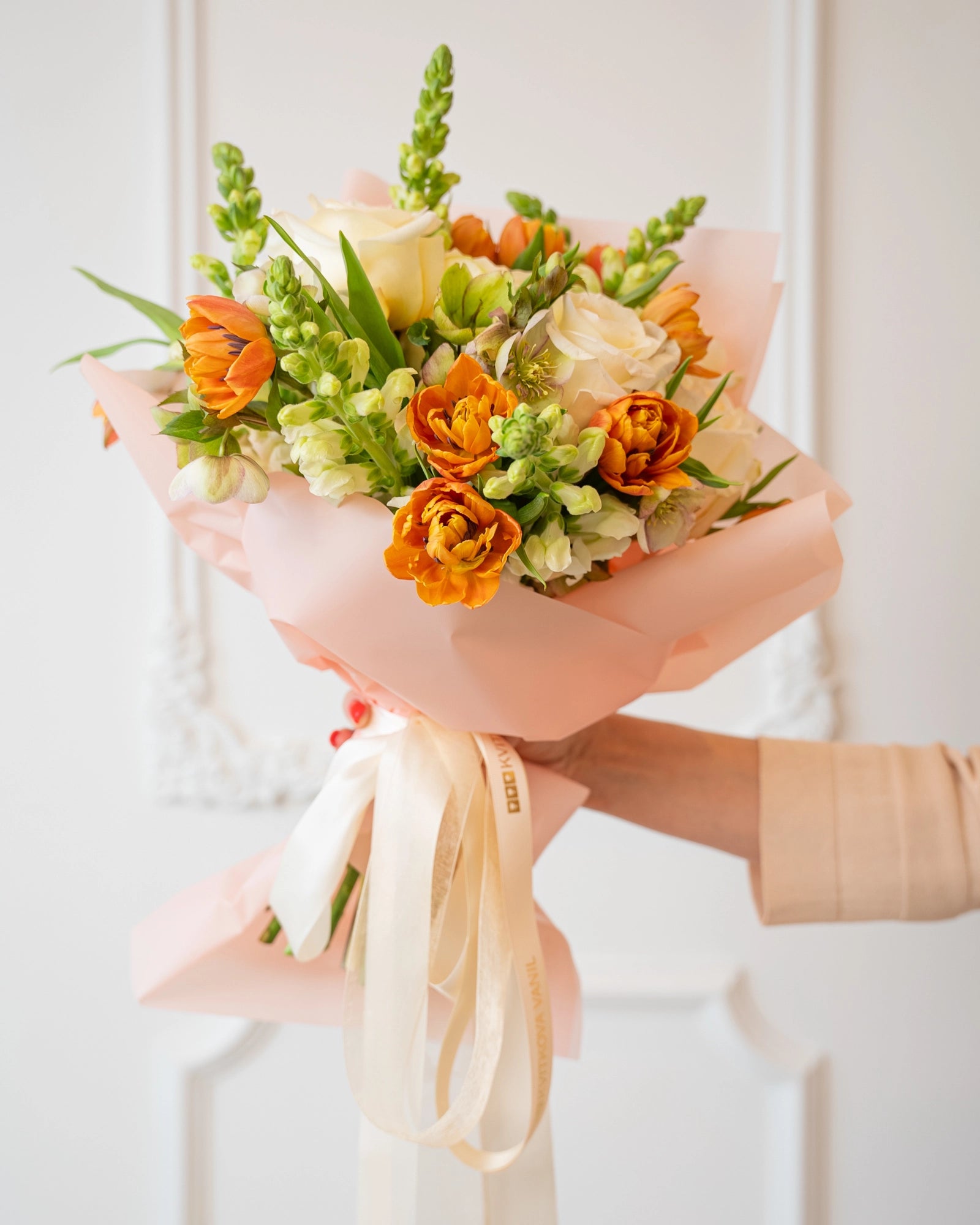 Detail shot of orange ranunculus and pale filler blossoms with soft ribbon accents