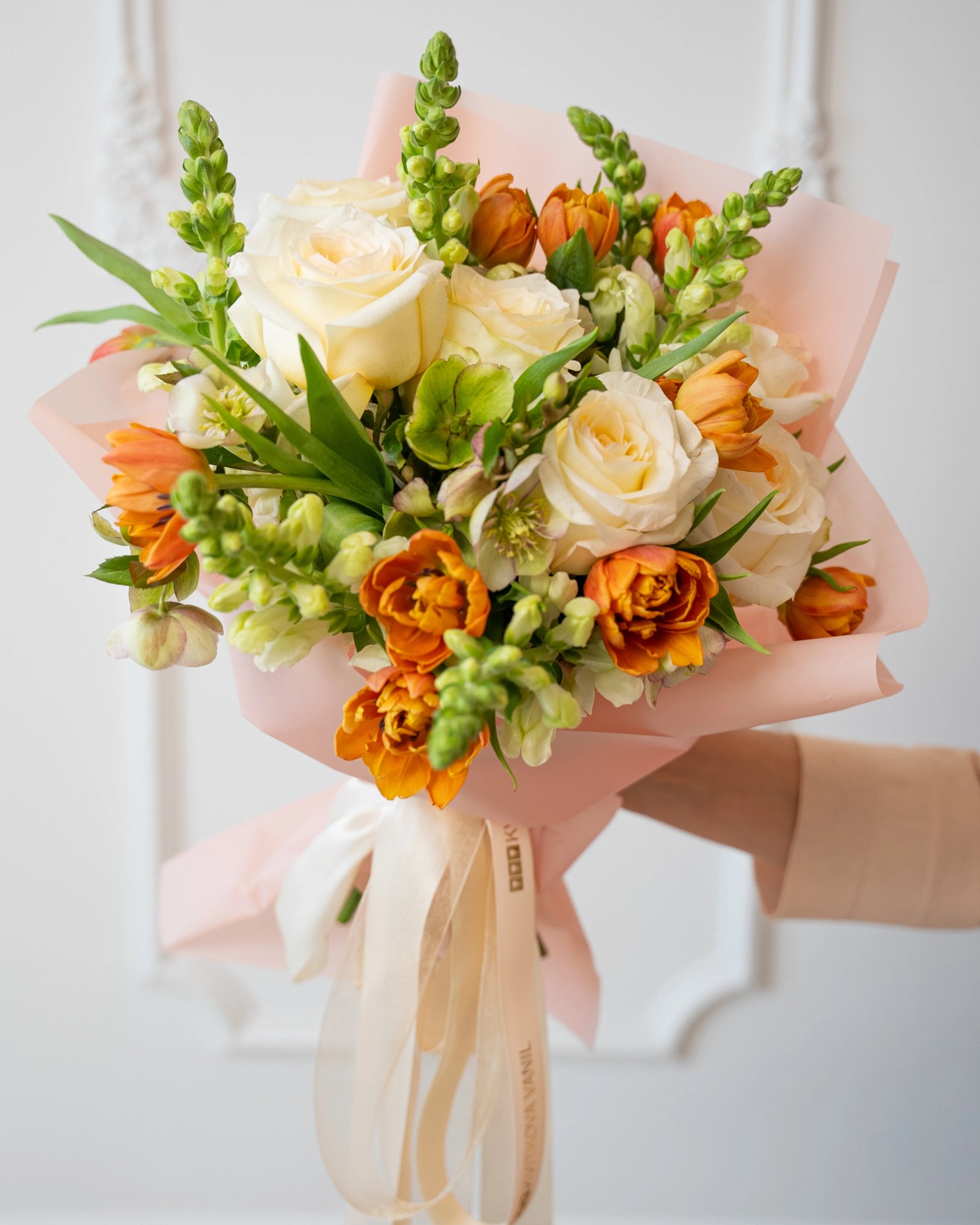 Side view showing layered ranunculus, snapdragon buds, and cream roses in a blush paper wrap