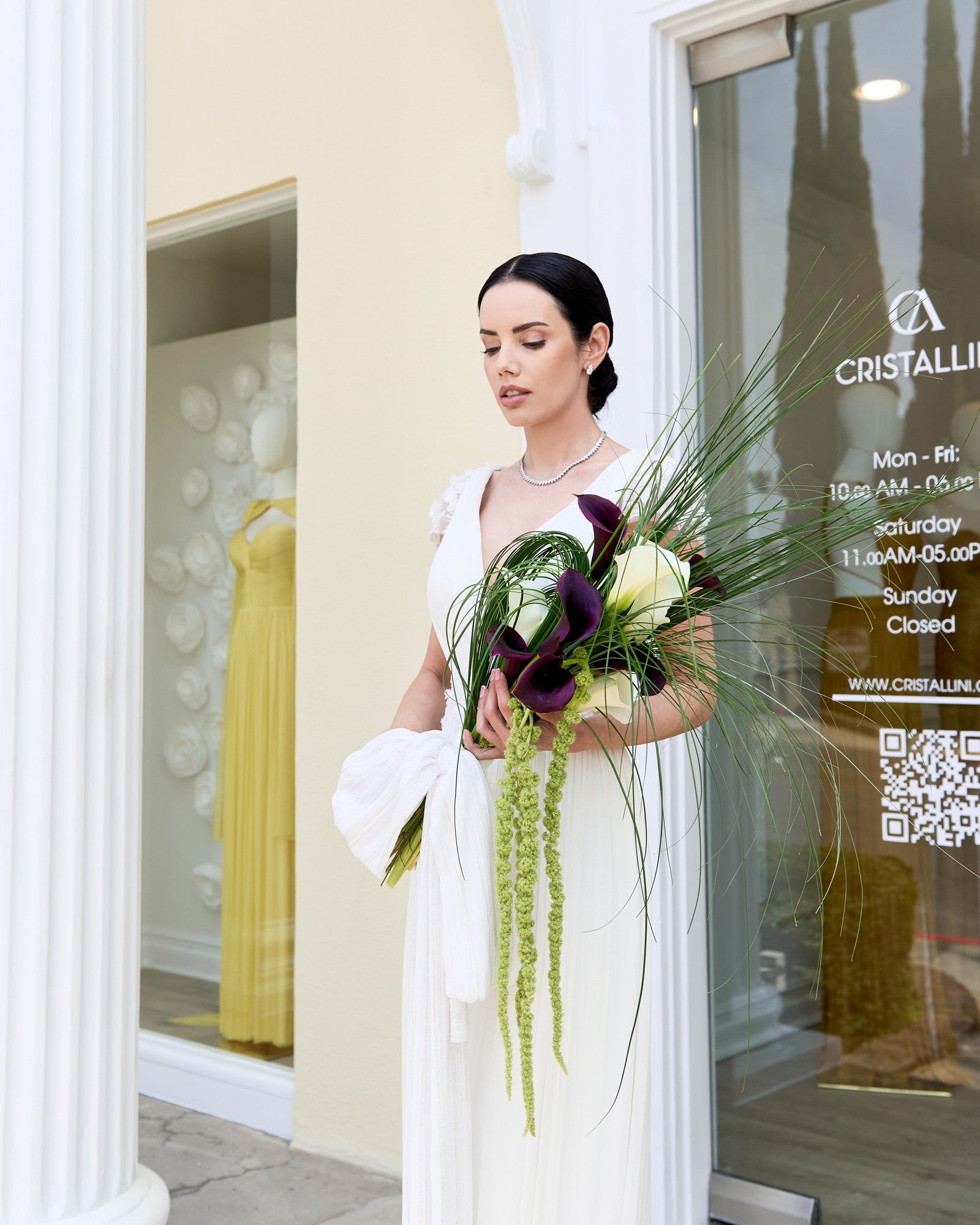 Modern bridal bouquet featuring deep burgundy and ivory calla lilies, cascading green amaranthus, and sculptural bear grass, held by an elegant bride.